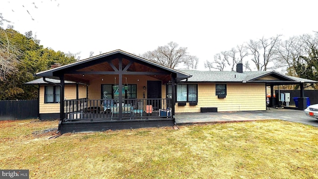 view of front of house featuring fence, covered porch, a chimney, a carport, and a lawn