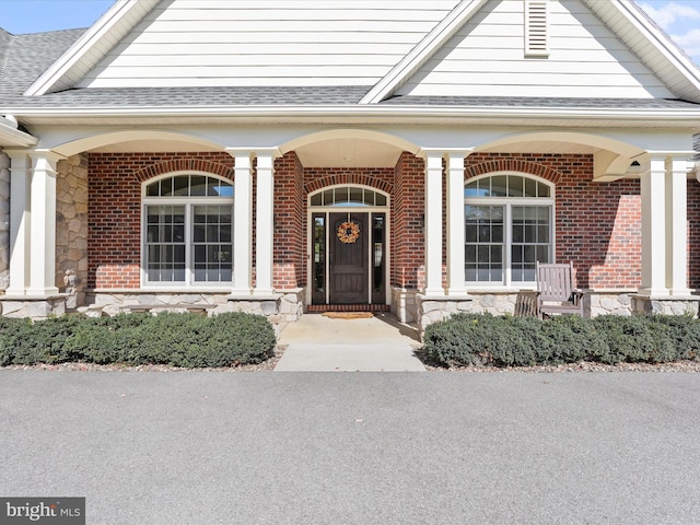 property entrance with stone siding, a shingled roof, a porch, and brick siding