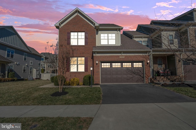 view of front of home featuring driveway, a lawn, roof with shingles, an attached garage, and brick siding