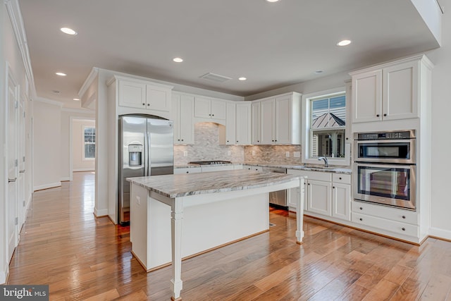 kitchen featuring appliances with stainless steel finishes, light wood-type flooring, a kitchen island, and decorative backsplash