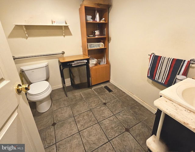 bathroom with stone finish flooring, toilet, vanity, and baseboards