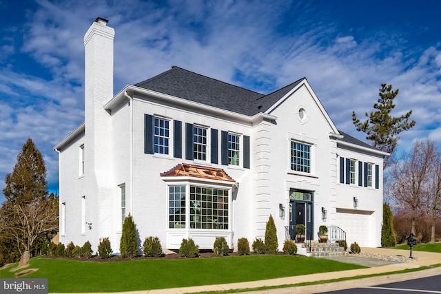 view of front of house with a shingled roof, a front yard, an attached garage, and a chimney