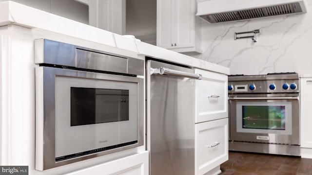 kitchen with stainless steel appliances, light stone countertops, range hood, and white cabinetry
