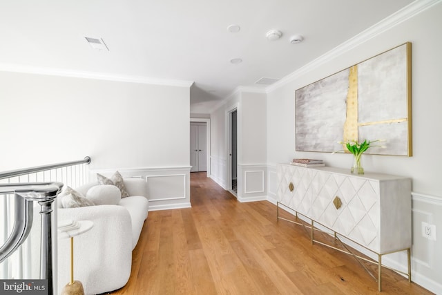 corridor featuring a wainscoted wall, visible vents, light wood-style flooring, crown molding, and a decorative wall
