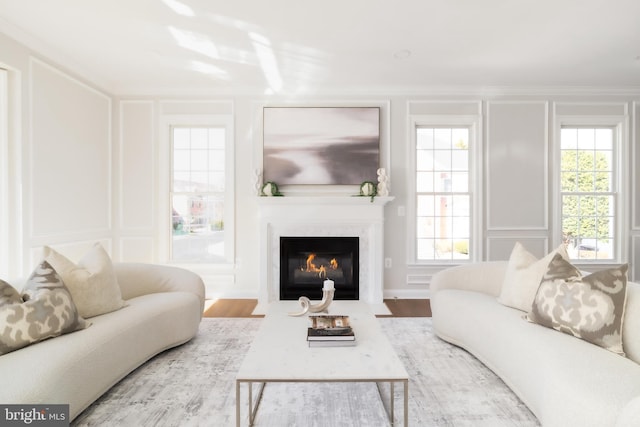 living room featuring wood finished floors, ornamental molding, a fireplace with flush hearth, and a decorative wall