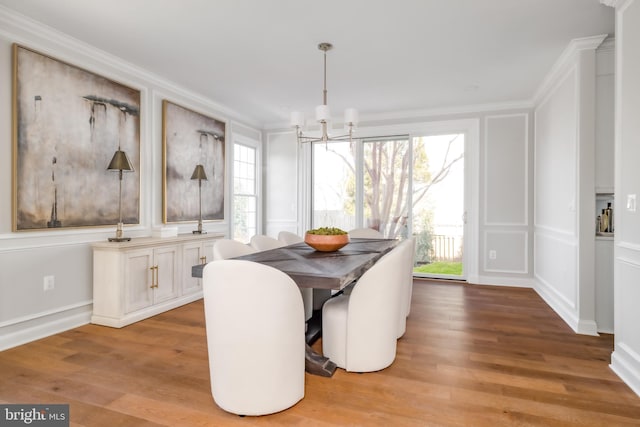 dining room with wood finished floors, a notable chandelier, ornamental molding, and a decorative wall
