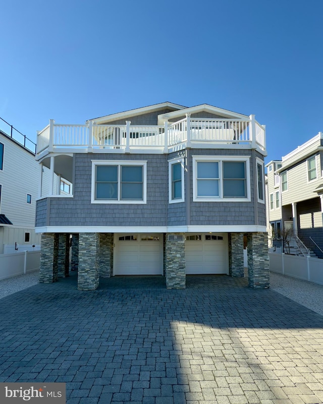 view of front of property with a garage, decorative driveway, a balcony, and stone siding