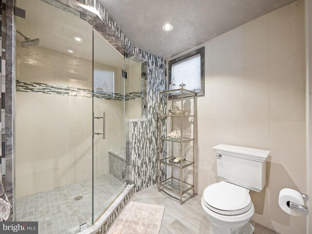 full bathroom featuring a stall shower, tile patterned floors, toilet, and tile walls