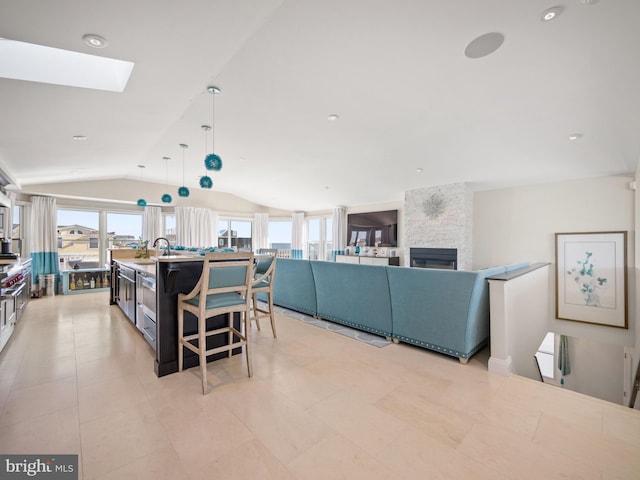 kitchen featuring light tile patterned floors, vaulted ceiling with skylight, a kitchen island with sink, a fireplace, and decorative light fixtures