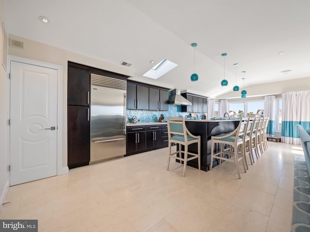 kitchen with a breakfast bar, visible vents, wall chimney range hood, lofted ceiling with skylight, and stainless steel built in refrigerator