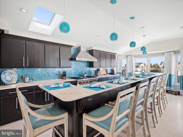 kitchen featuring light countertops, hanging light fixtures, stove, lofted ceiling with skylight, and wall chimney range hood