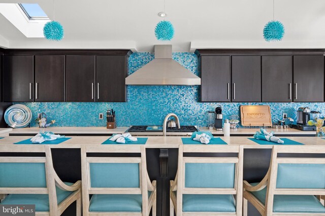 kitchen featuring tasteful backsplash, light countertops, wall chimney range hood, and a breakfast bar area