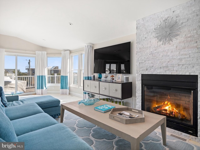 living area with lofted ceiling, visible vents, baseboards, and a stone fireplace