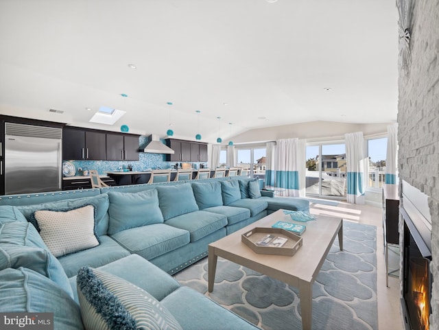 living area with lofted ceiling with skylight, visible vents, and a stone fireplace