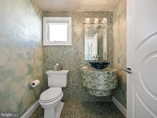 half bath with tile patterned flooring, baseboards, a sink, and toilet