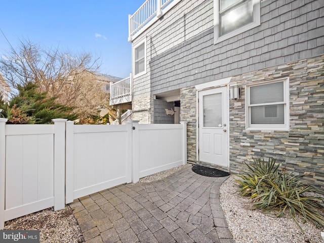 property entrance featuring a balcony, stone siding, a gate, and fence