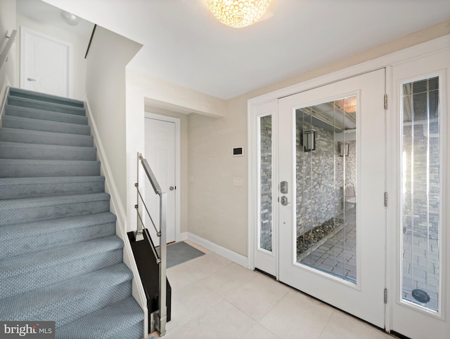 entryway featuring light tile patterned floors, baseboards, and stairs