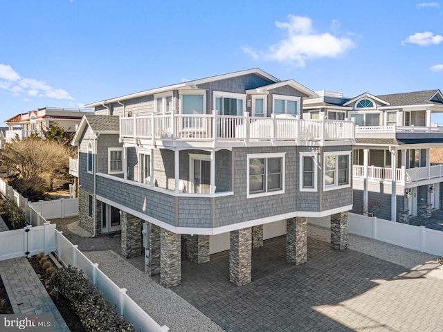 exterior space featuring a balcony, stone siding, a fenced backyard, and a gate