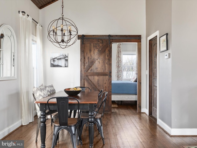 dining area featuring dark wood-style floors, a barn door, an inviting chandelier, high vaulted ceiling, and baseboards