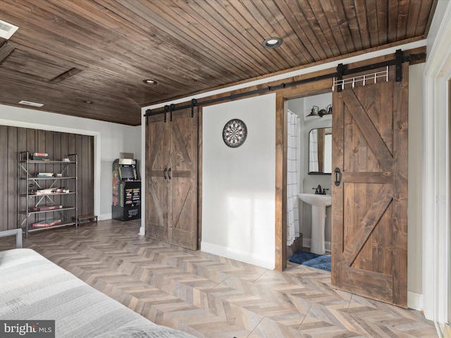 unfurnished bedroom with a barn door, baseboards, wooden ceiling, ensuite bathroom, and a sink