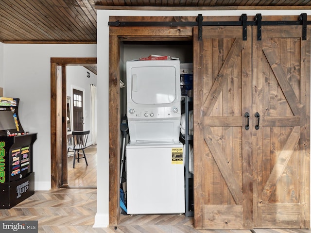 laundry area with laundry area, baseboards, stacked washing maching and dryer, and a barn door