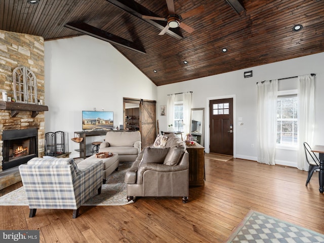 living room featuring high vaulted ceiling, a barn door, hardwood / wood-style flooring, and a stone fireplace