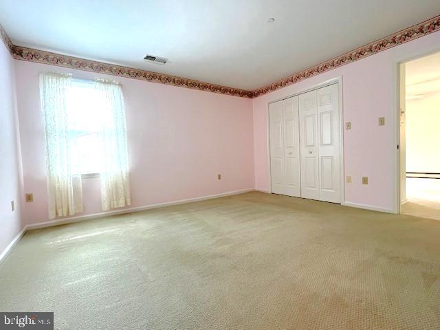 unfurnished bedroom with a closet, visible vents, light carpet, and baseboards