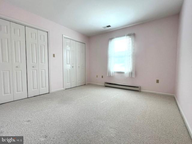 unfurnished bedroom featuring a baseboard heating unit, baseboards, two closets, and light colored carpet