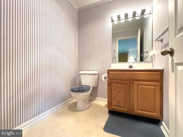 bathroom with baseboards, vanity, toilet, and wallpapered walls