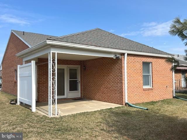 back of house featuring a patio area, a shingled roof, a yard, and brick siding