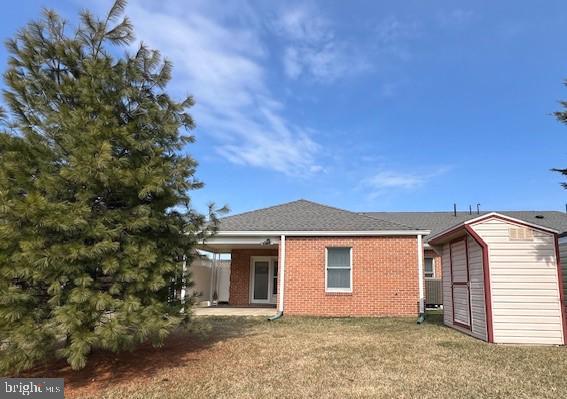 back of property featuring a storage shed, brick siding, a lawn, and an outdoor structure