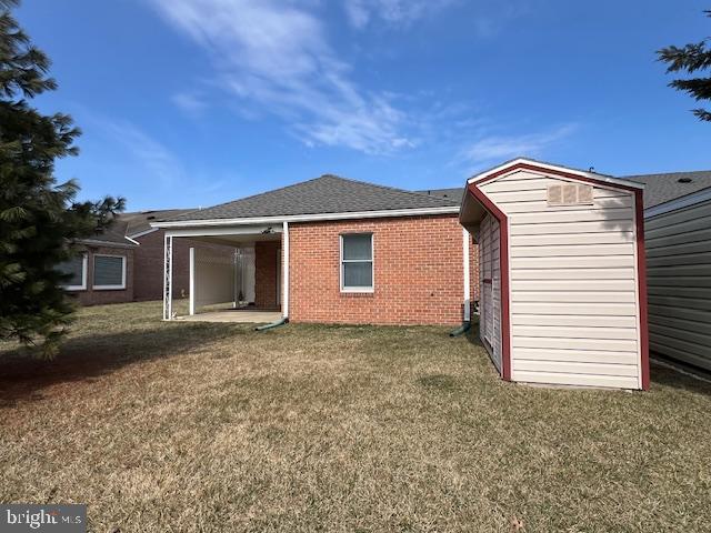 back of house with a storage shed, roof with shingles, a yard, an outdoor structure, and brick siding