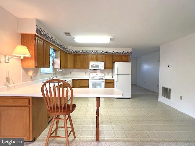 kitchen with white appliances, visible vents, light countertops, and brown cabinetry