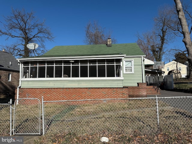 rear view of house with a gate, a sunroom, a chimney, and fence