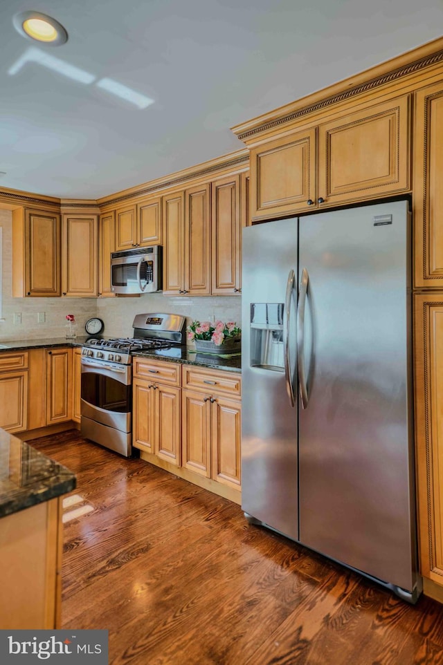 kitchen featuring stainless steel appliances, dark wood finished floors, dark stone countertops, and tasteful backsplash