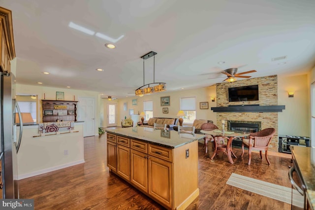 kitchen with stone counters, a large fireplace, open floor plan, dark wood-style floors, and brown cabinetry