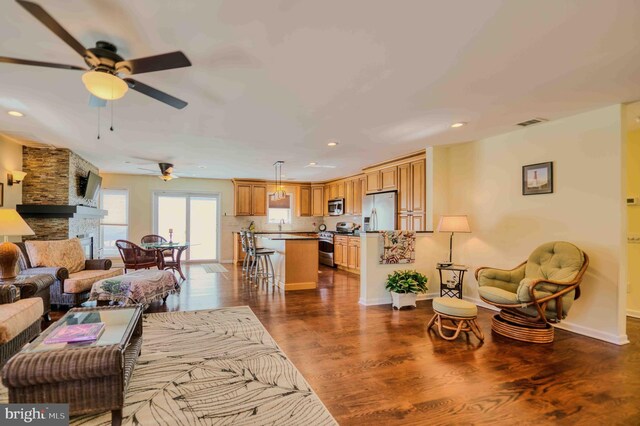 living area featuring a stone fireplace, recessed lighting, visible vents, baseboards, and dark wood finished floors