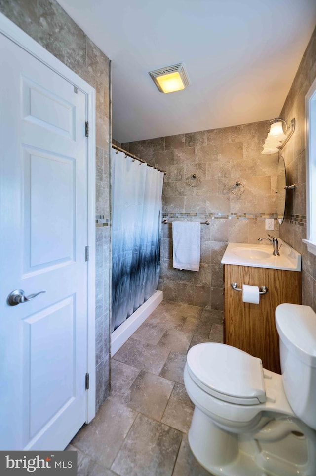 full bath with tile walls, stone tile flooring, a shower with shower curtain, toilet, and vanity