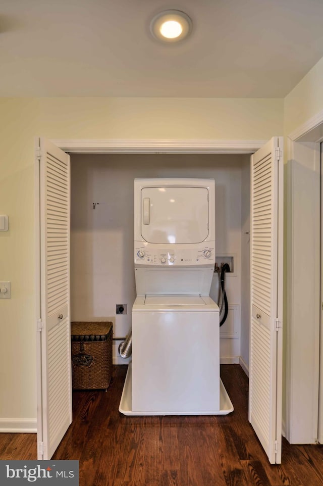 laundry room featuring stacked washer and dryer, baseboards, laundry area, and wood finished floors