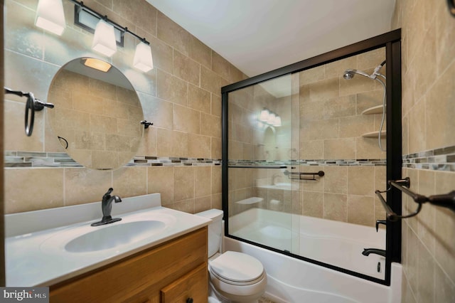 bathroom featuring toilet, bath / shower combo with glass door, vanity, and tile walls