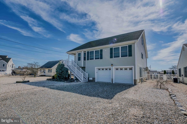 view of front of house with central AC unit, an attached garage, fence, stairway, and gravel driveway