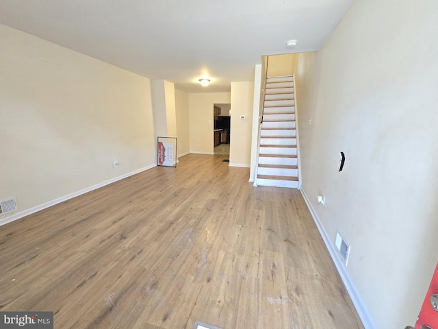 unfurnished living room featuring light wood-type flooring, baseboards, stairs, and visible vents