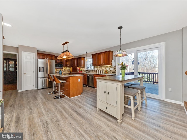 kitchen with a breakfast bar, backsplash, stainless steel appliances, and light wood-type flooring