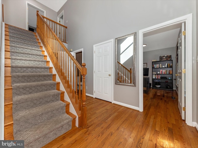 stairs with baseboards, a high ceiling, and wood finished floors