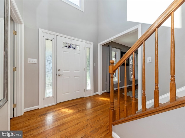 entrance foyer with stairway, baseboards, a high ceiling, and light wood finished floors