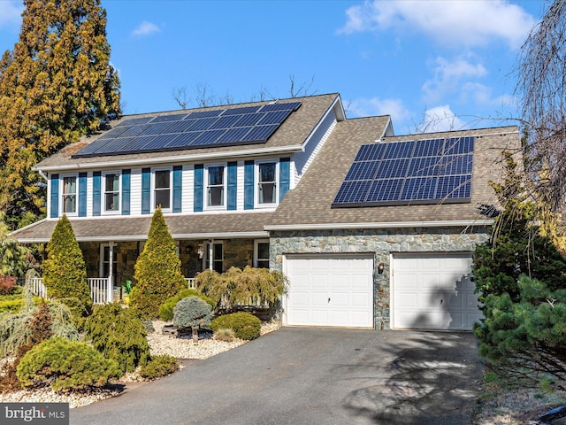 view of front of property with stone siding, an attached garage, driveway, and roof with shingles