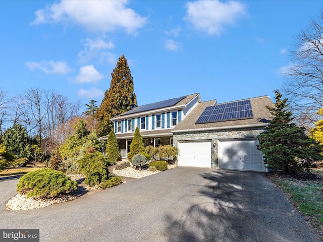 view of front of home with aphalt driveway, a garage, stone siding, and roof mounted solar panels