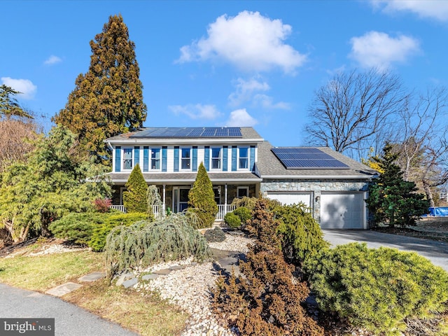 view of front of house with aphalt driveway, stone siding, roof mounted solar panels, covered porch, and an attached garage