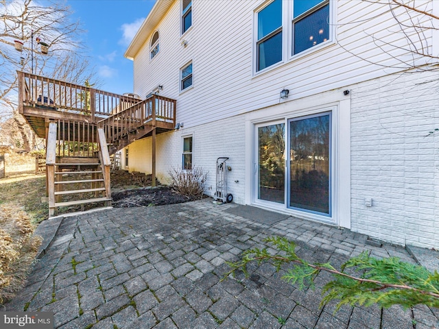 rear view of property with a deck, a patio, stairway, and brick siding