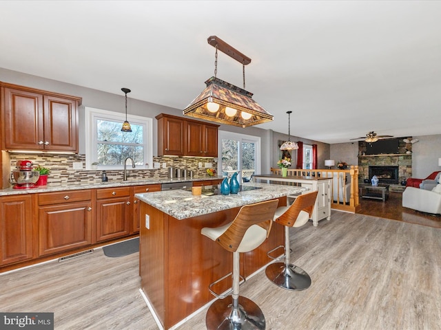 kitchen with light wood-type flooring, visible vents, a kitchen island, backsplash, and light stone countertops